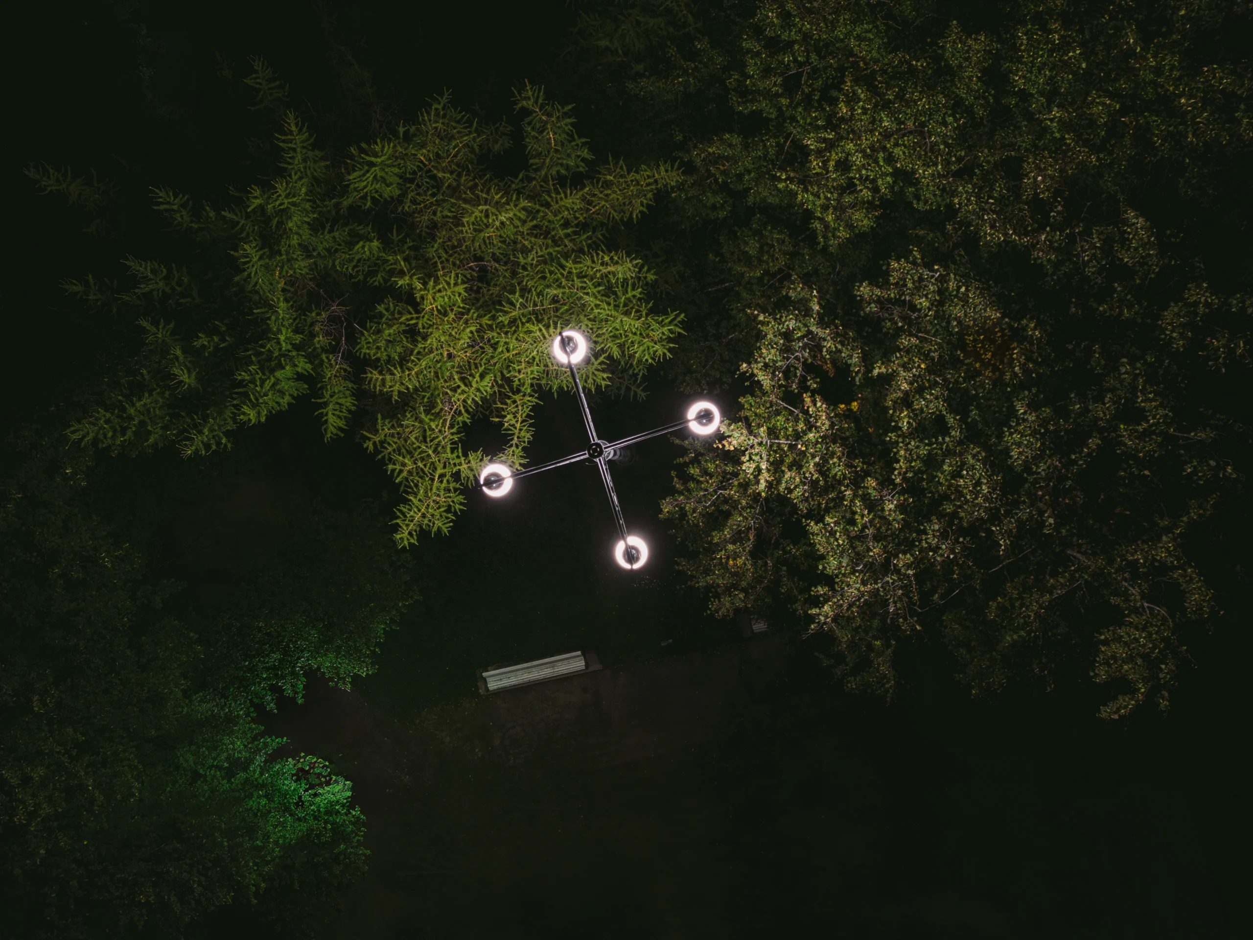 Overhead nighttime view of an energy-efficient LED street lamp surrounded by trees in a park.