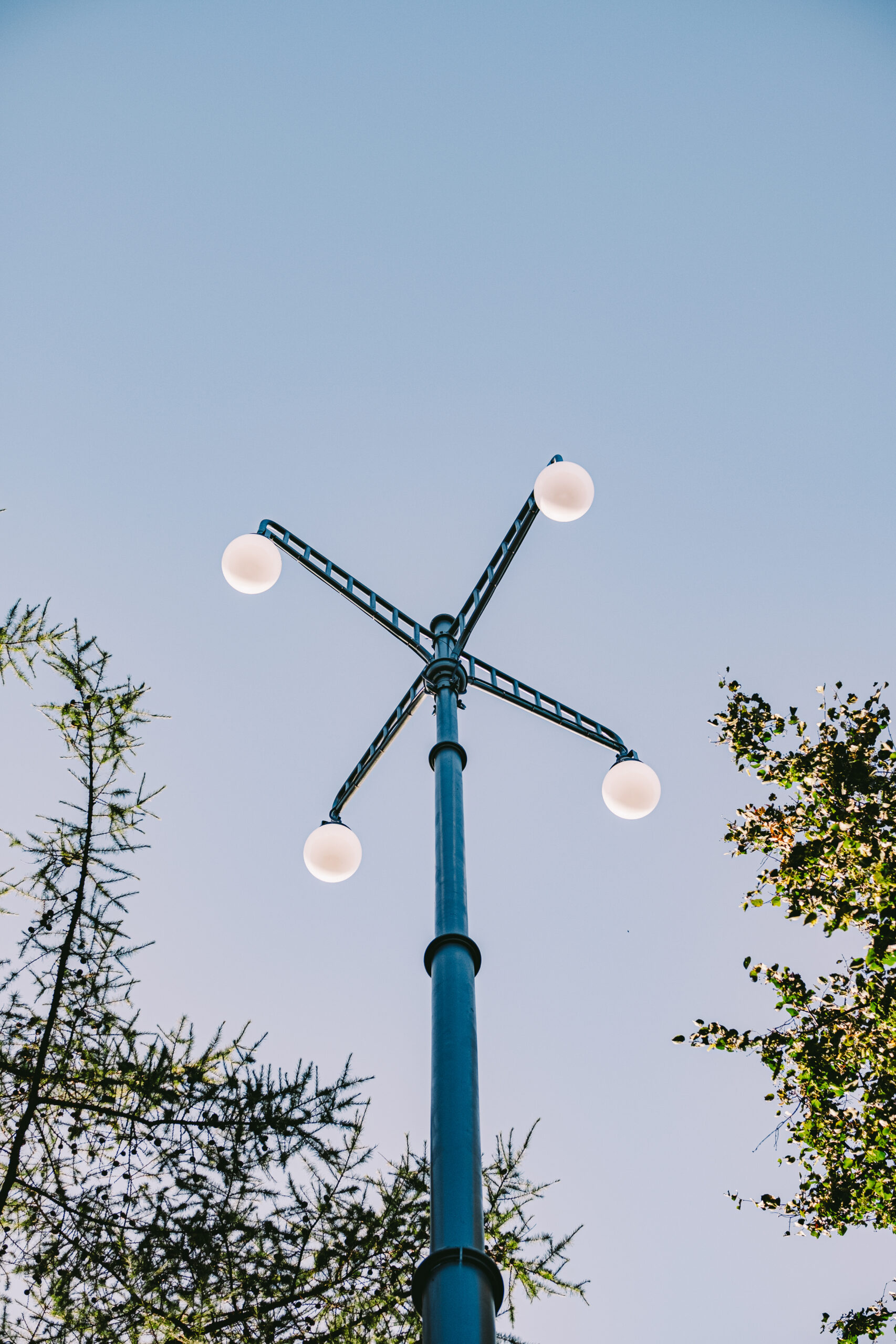 A view from the ground up to a historical outdoor park light on a sunny summer day with blue sky and green trees.