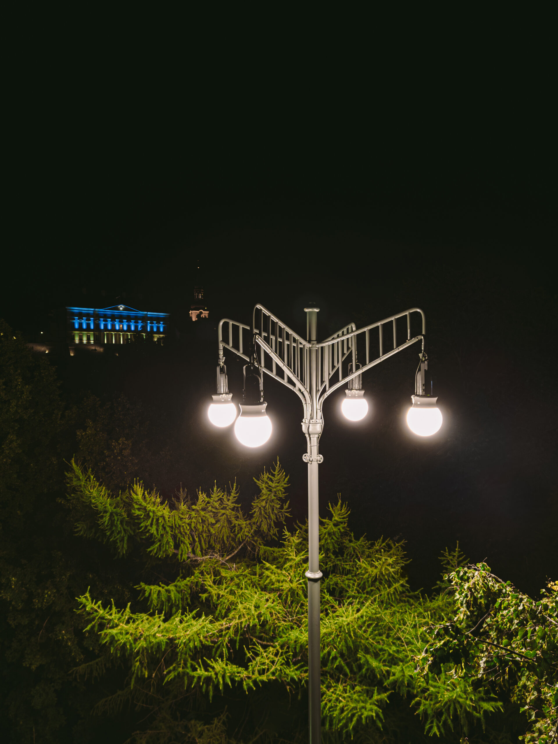 Nighttime view of a lit bespoke historic street lamp, with the Estonian Parliament in the background illuminated in Ukrainian flag colors