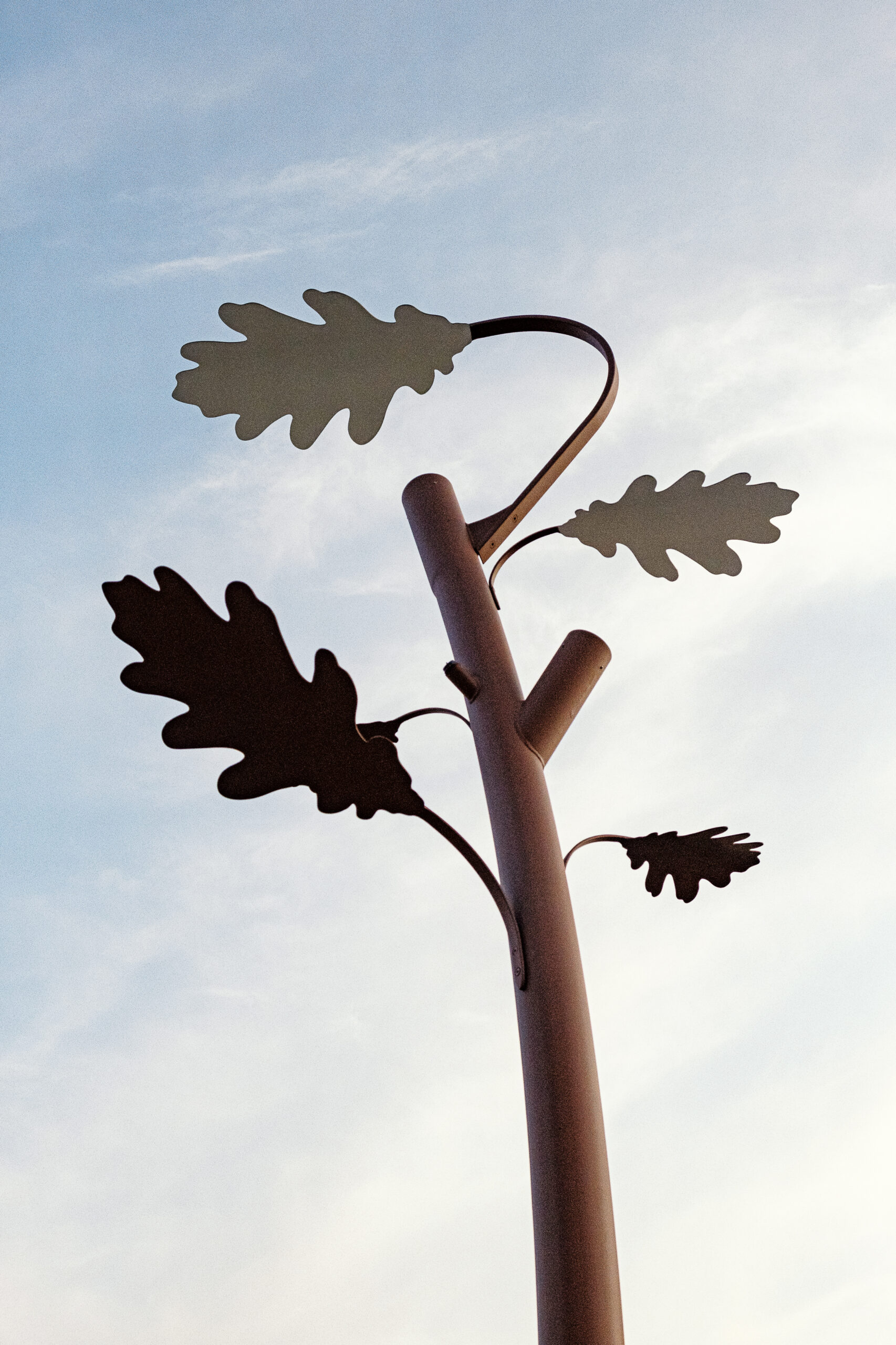 Close-up of a metal oak tree shaped outdoor pole light with leaf-shaped elements against a clear sky background