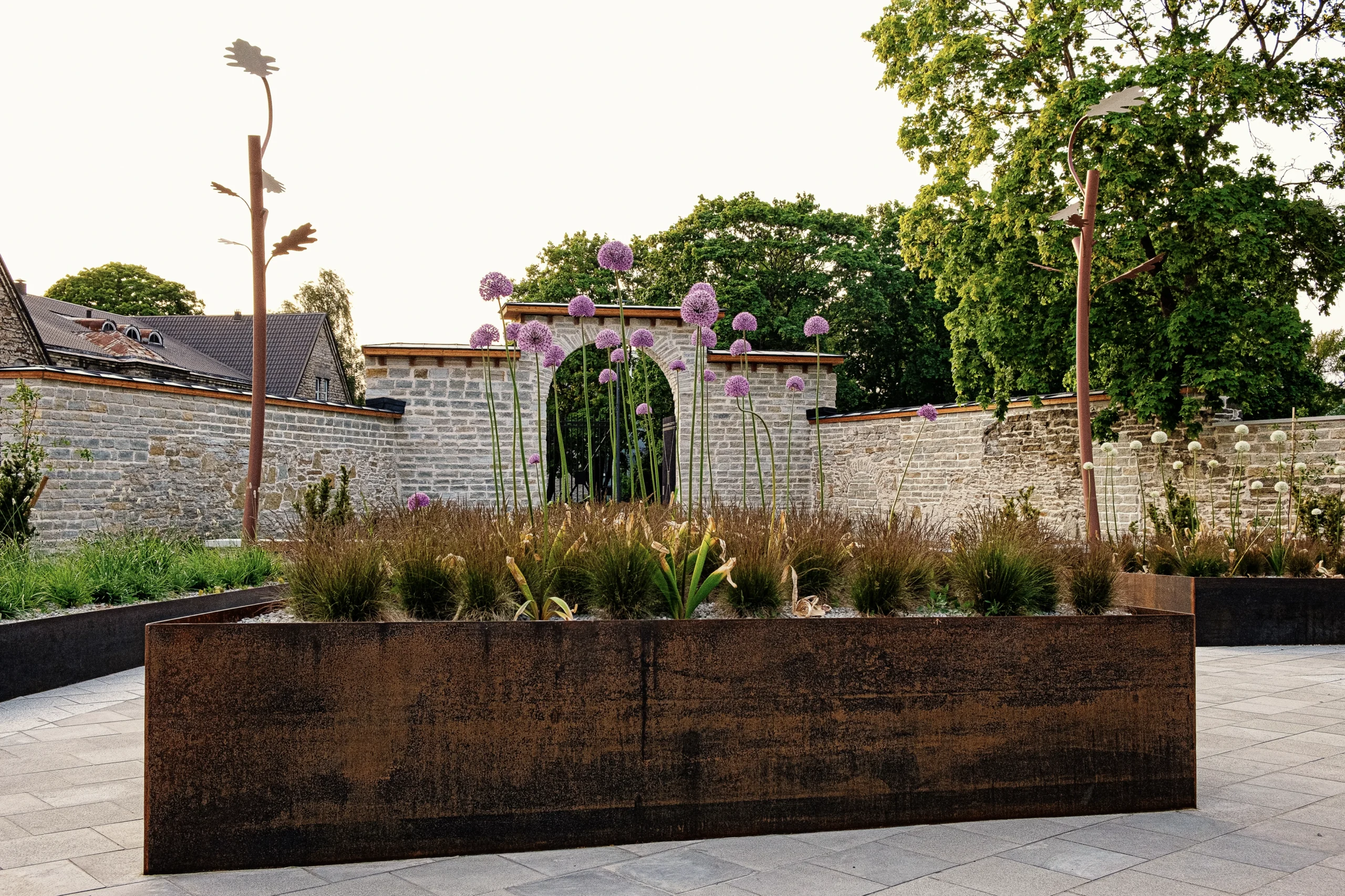 Modern garden featuring oak tree-shaped outdoor lights, purple flowers, and a stone wall.