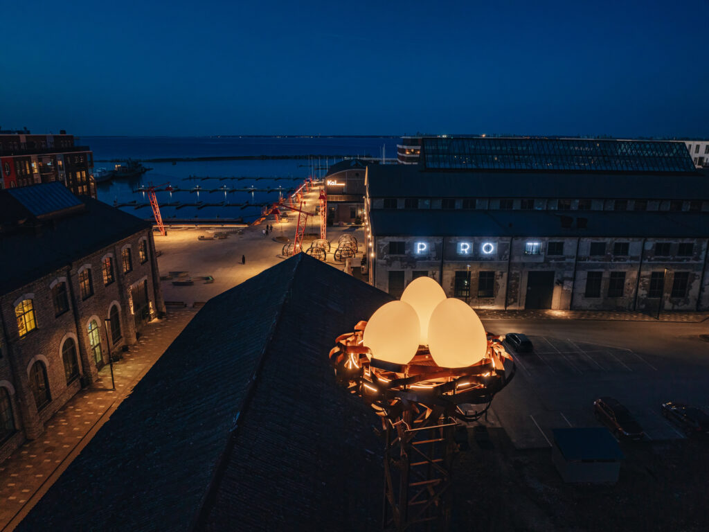 Nighttime view of a nest eggs lighting art installation on a tower, overlooking a waterfront industrial area