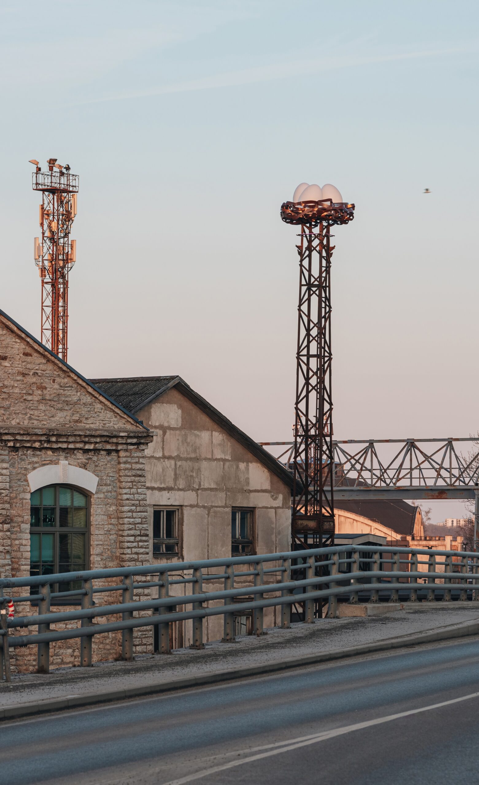 Industrial area at dawn with historic buildings, a tall chimney, and a nature-inspired nest eggs lighting art installation