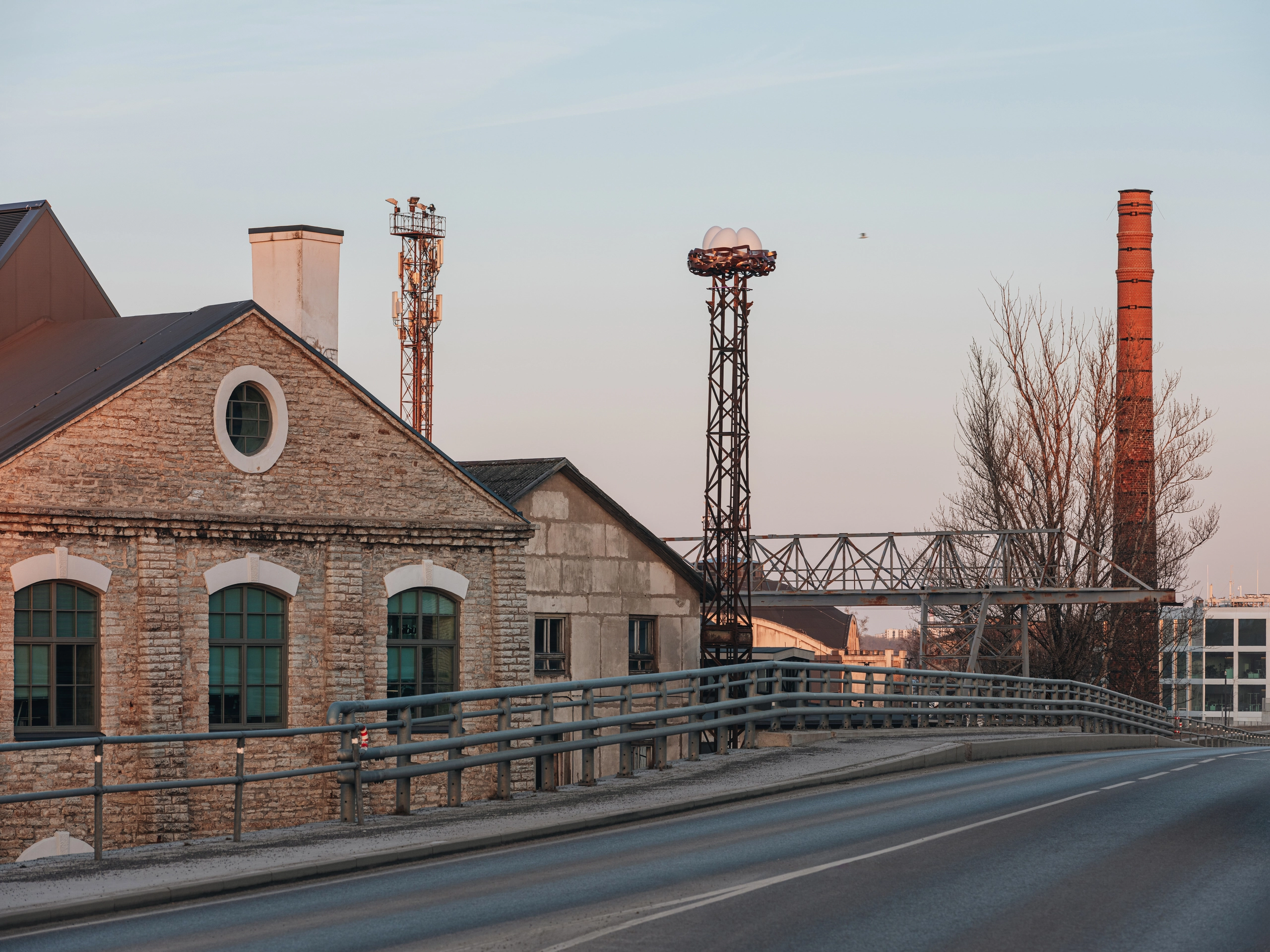 NEST urban light installation glowing at dawn in a historic industrial area, featuring old buildings and a tall chimney.