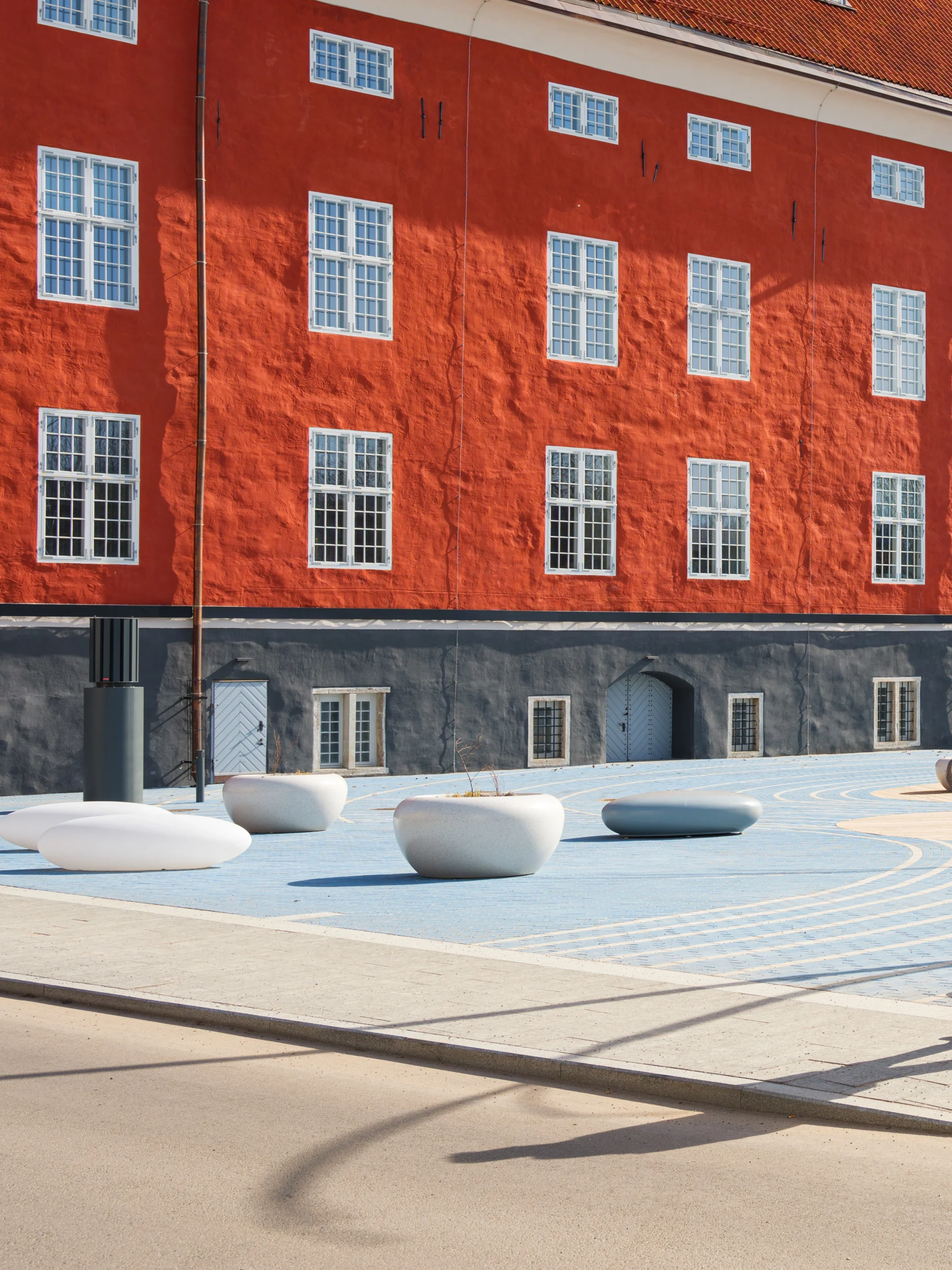 Urban courtyard featuring urban seating with pebble-inspired design near a red historical building.