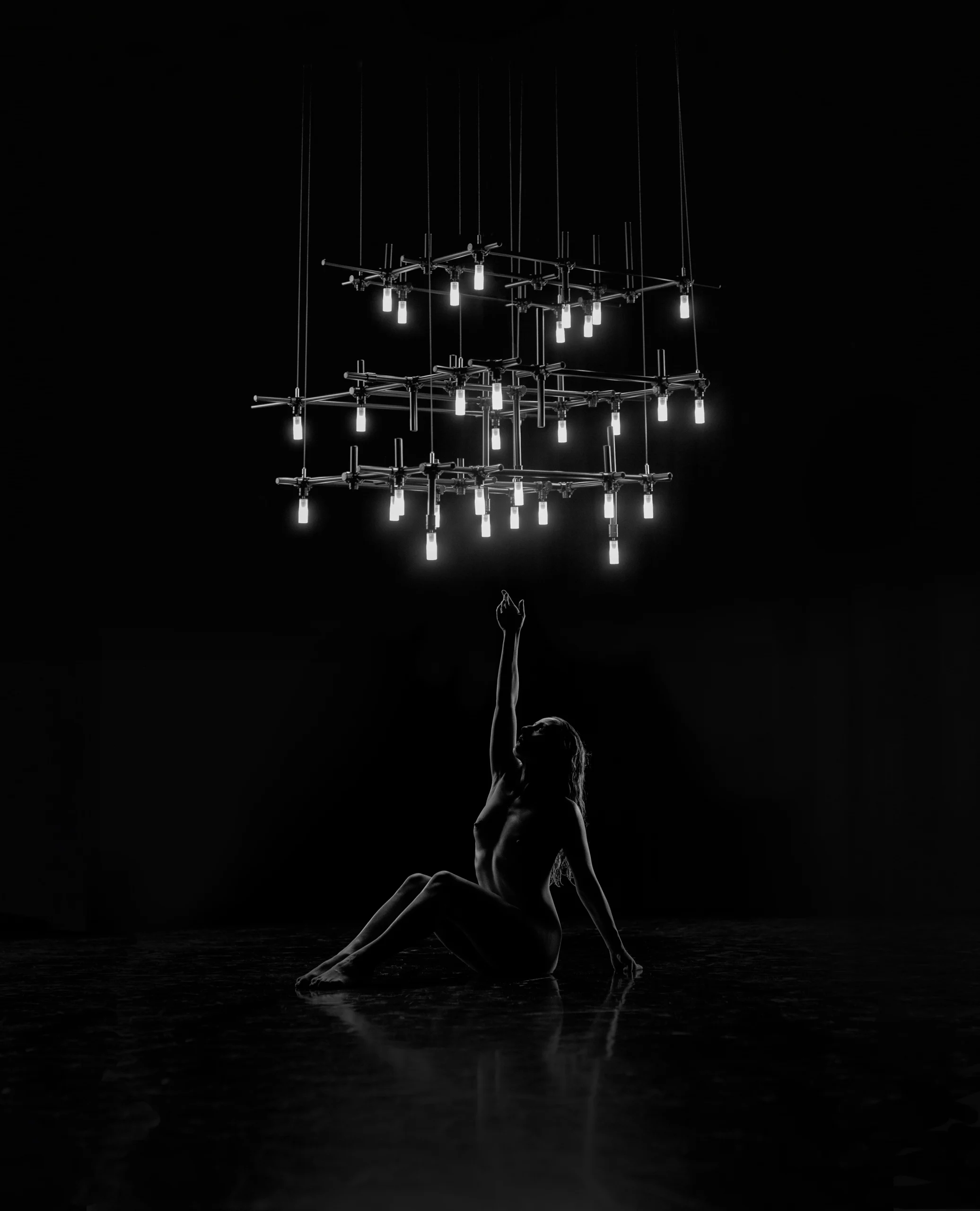 Monochrome image of a dancer interacting with HEXA architectural pendant light, reflecting on a glossy floor.