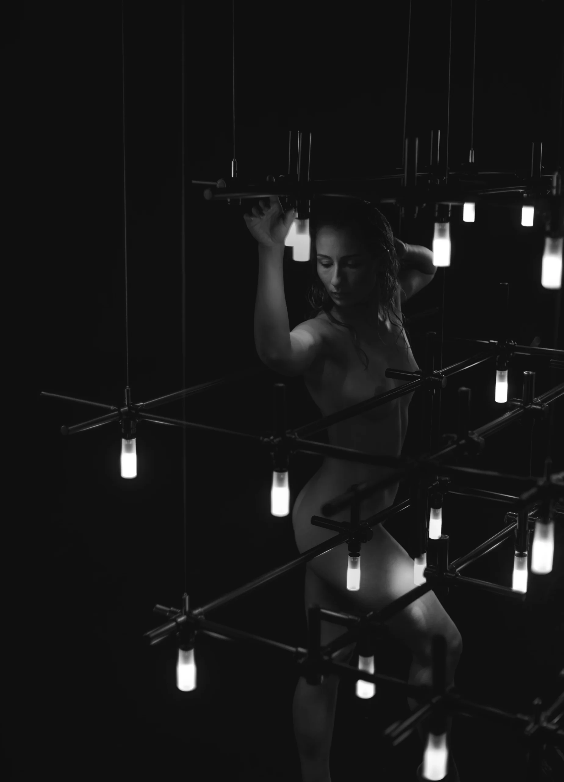 Monochrome image of a woman adjusting HEXA industrial chandelier with glowing glass bulbs.