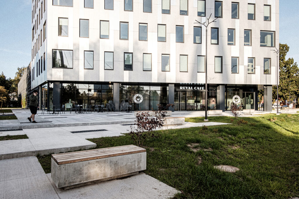 Paju office building facade with the Reval Cafe and plaza benches, a person walking, Tartu
