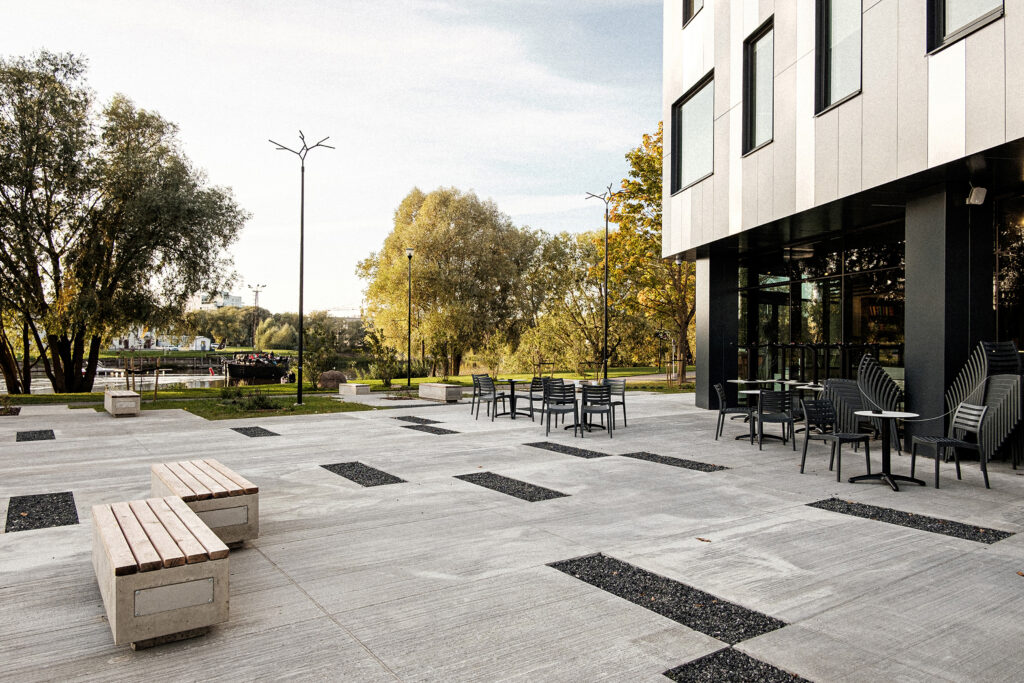 Branch luminaires over a paved plaza with benches beside the river at Paju, Tartu