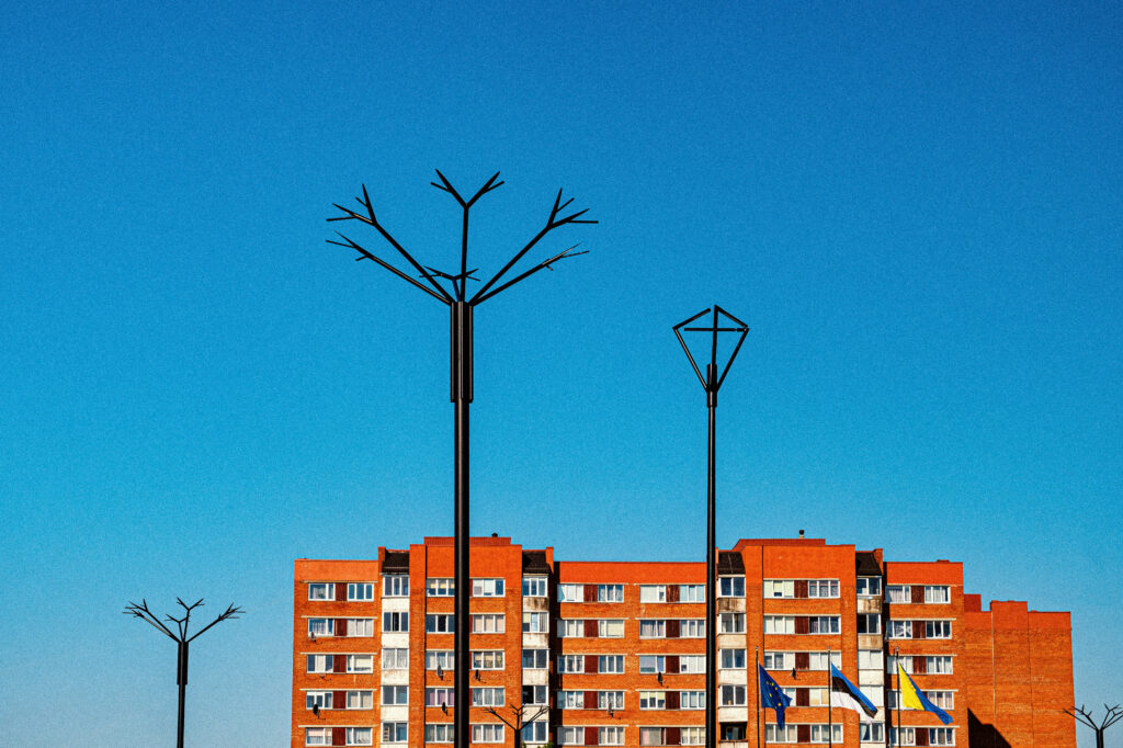 Looking up at Cornflower branching poles and a City lamp against deep blue sky, the square's pole-top lighting
