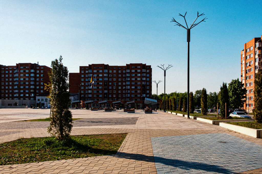 Cornflower poles line Ahtme's wide open public square, pedestrian street lighting receding toward the buildings