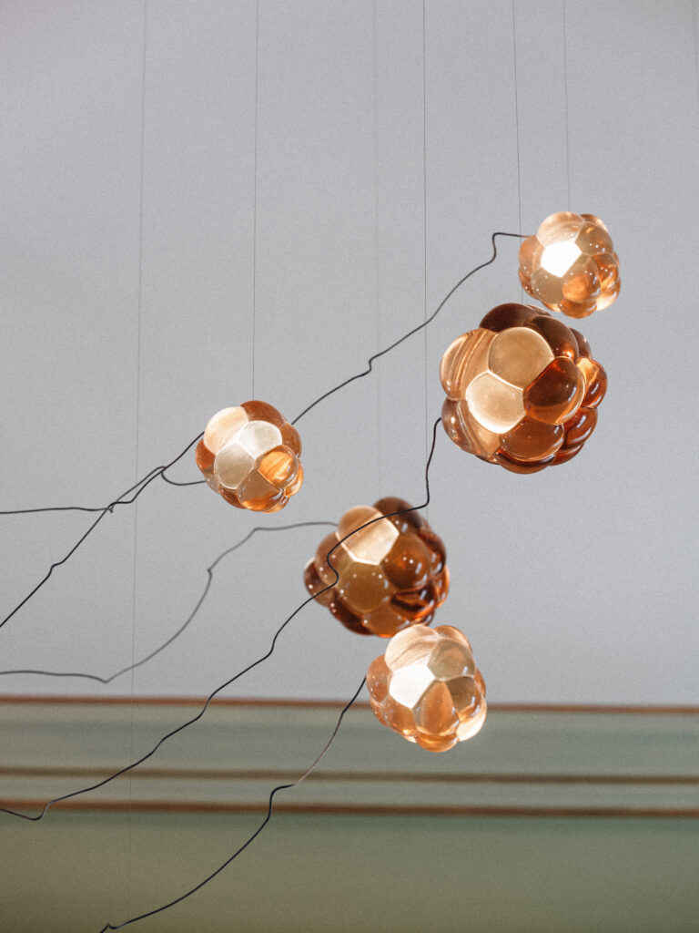 Cast resin Cloudberry pendants scattered on fine cables against a grey-green cornice, Berlin