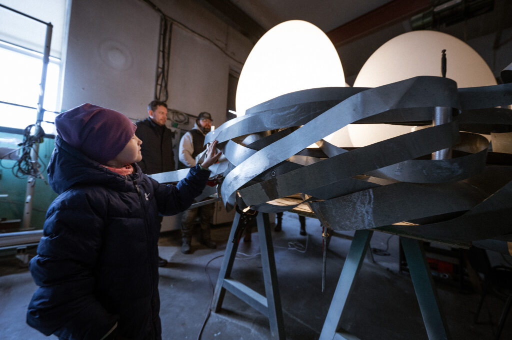 Child touching the woven metal Nest and its egg forms during fabrication, Tallinn