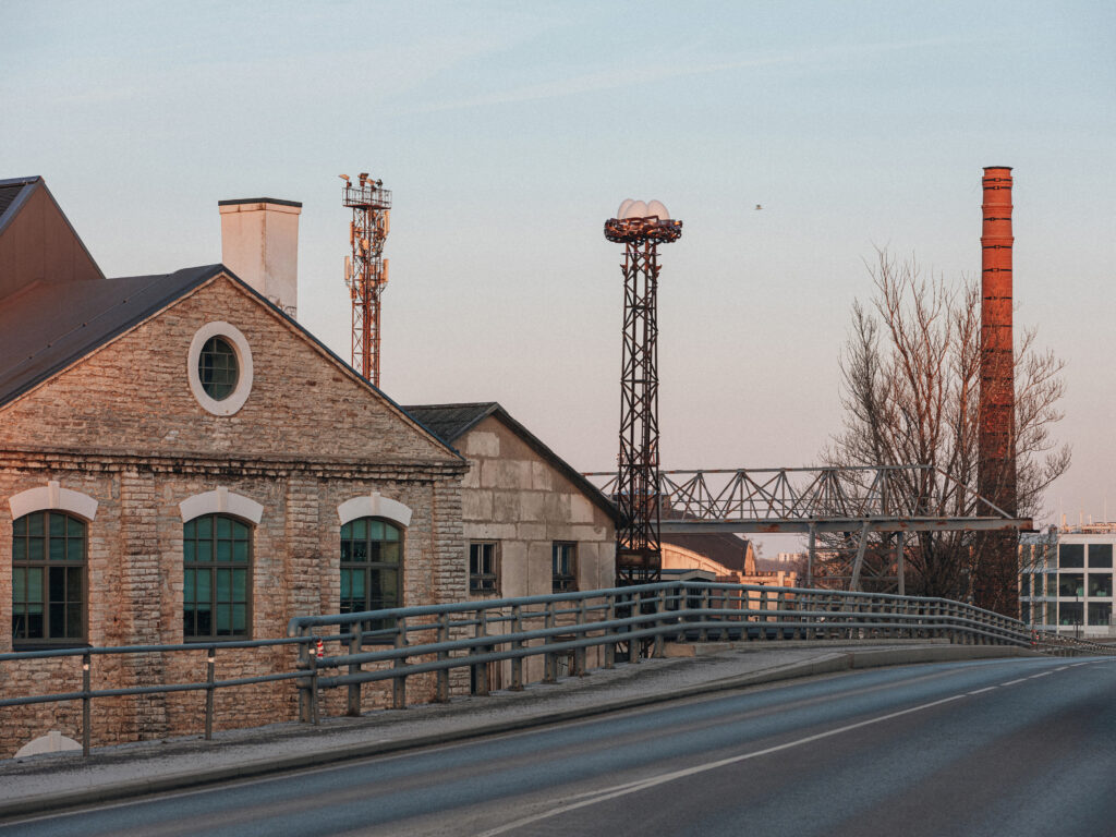 Nest on its tower above an old brick building and chimney at golden hour, Tallinn