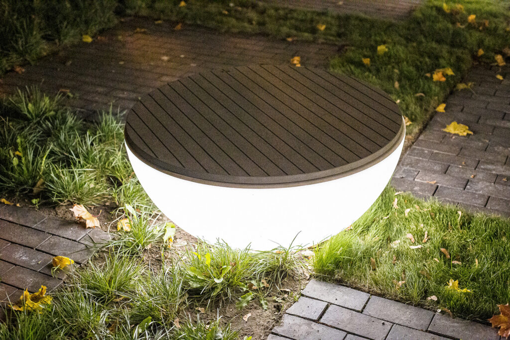 Timpan bench glowing from within at dusk, teak top above a lit polyethylene bowl, Tartu