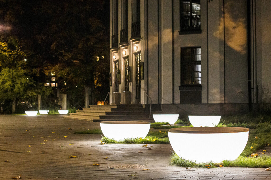 Row of illuminated Timpan benches leading to a lit building entrance at night, Tartu