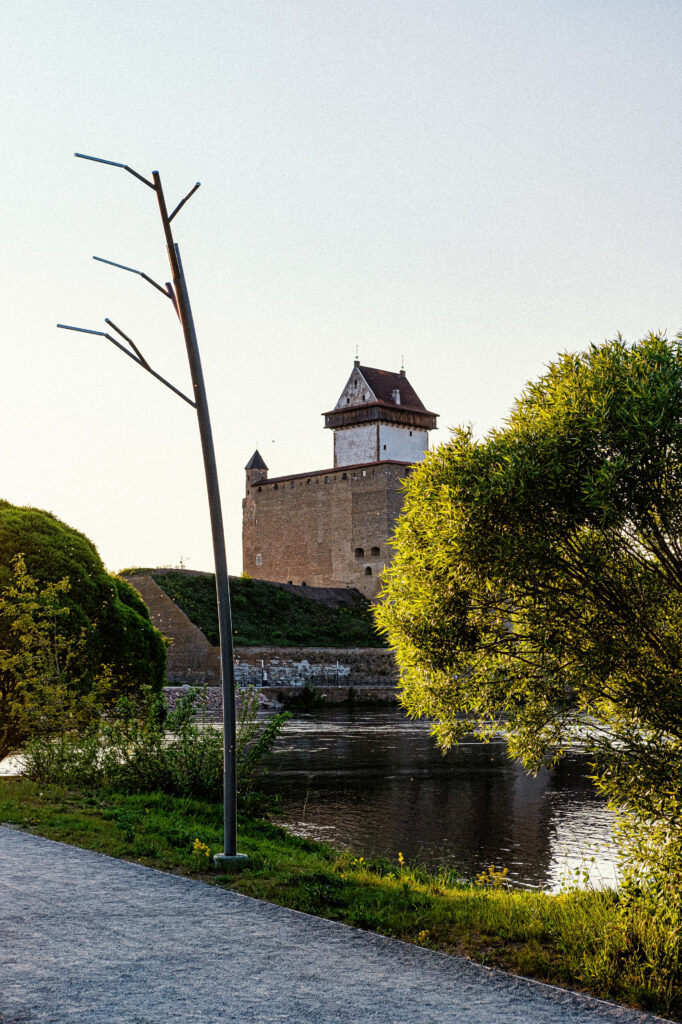 Tree luminaire by the river with Narva Castle tower across the water, Narva