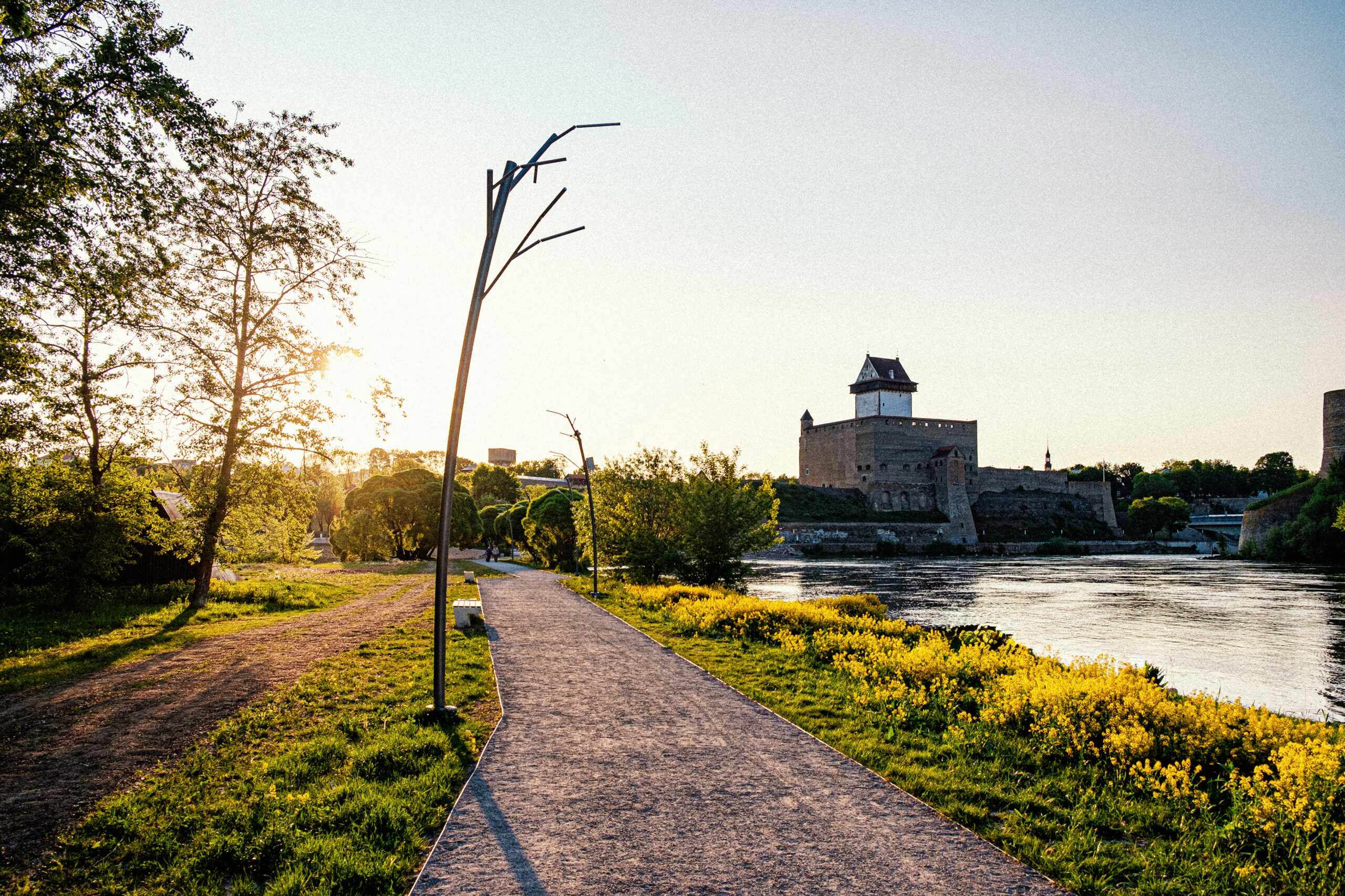 Tree luminaire on the Narva riverside promenade with Narva Castle at sunset