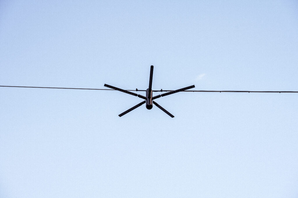 Blackbird catenary light seen from directly below in daylight, five LED profiles fanning out from the wire
