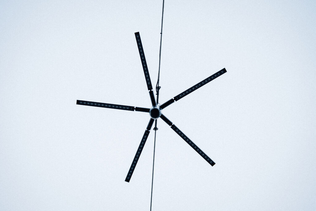 Underside of an unlit Blackbird catenary light against a white overcast sky, the LED chips visible along its five profiles