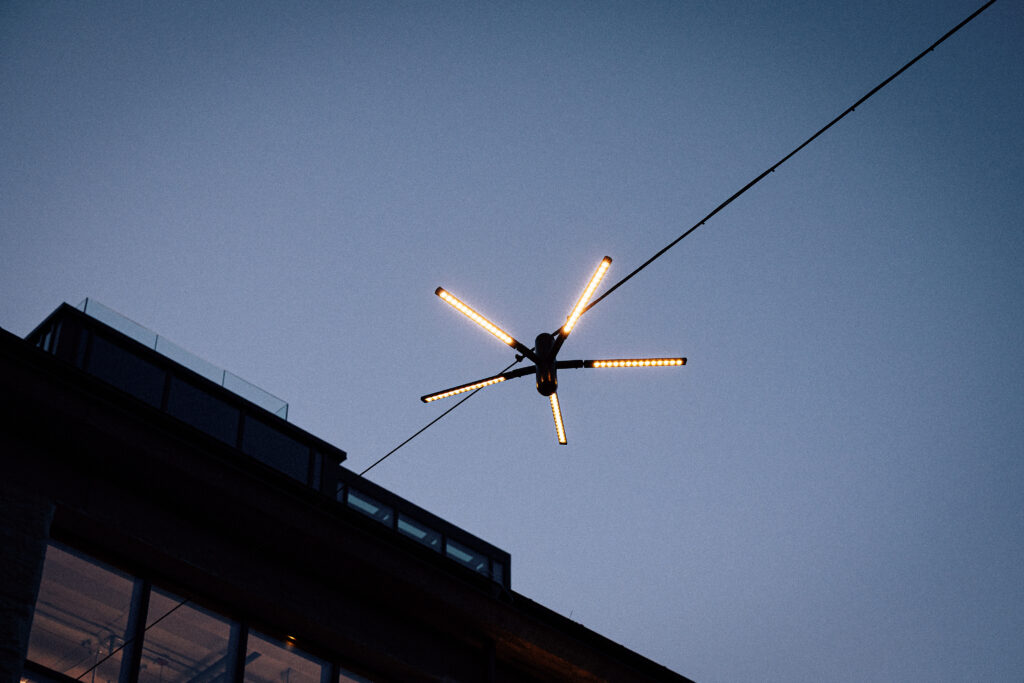 Blackbird hanging street light switched on at dusk, its wire running down past the rooftop of a Krulli Park building