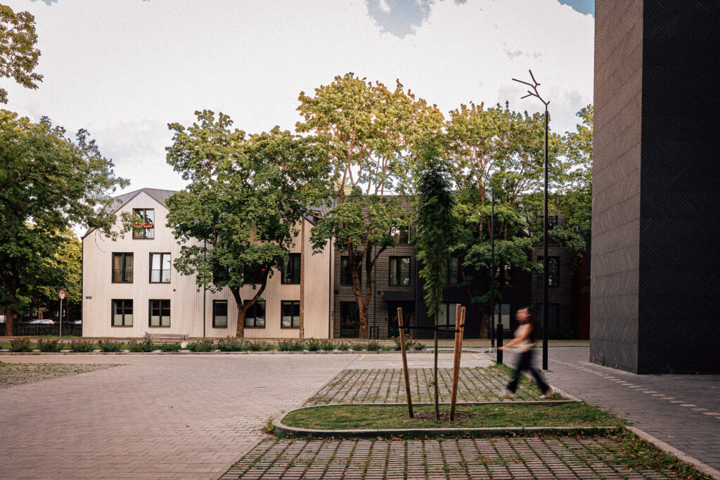 A pedestrian passes a Branch pole light at the edge of the Krulli Park parking area, mature trees and houses behind