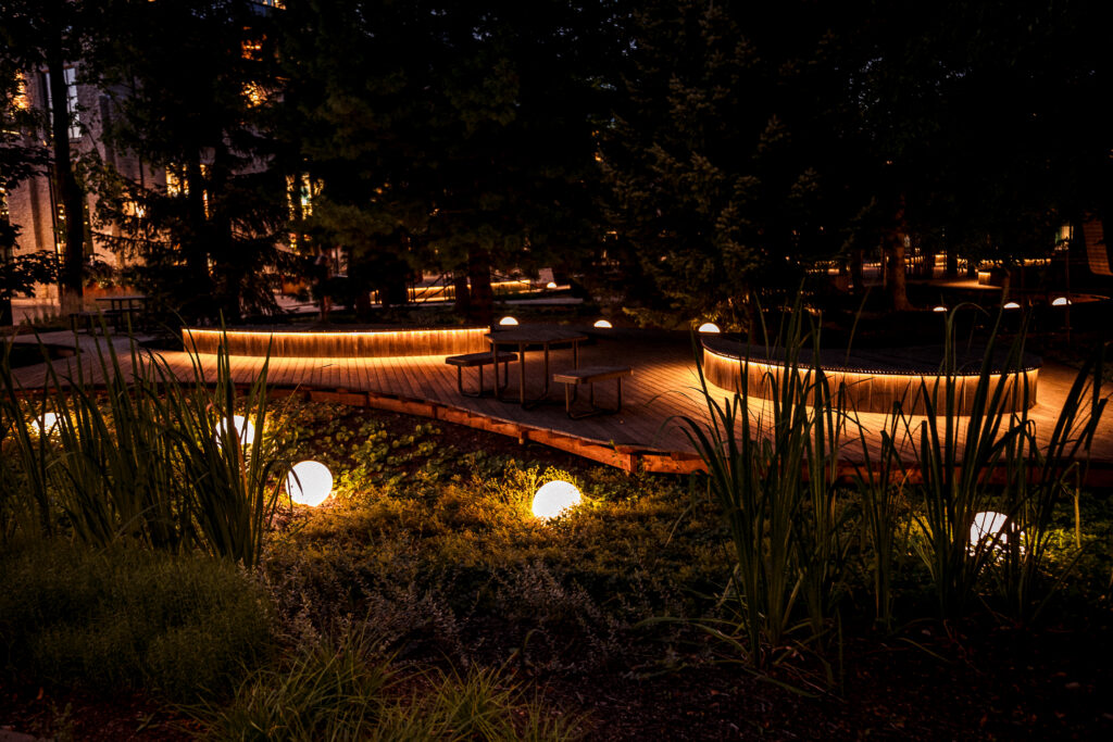 Buoy outdoor globe lights glowing in the planting at night, warm light washing out from under the raised timber decks