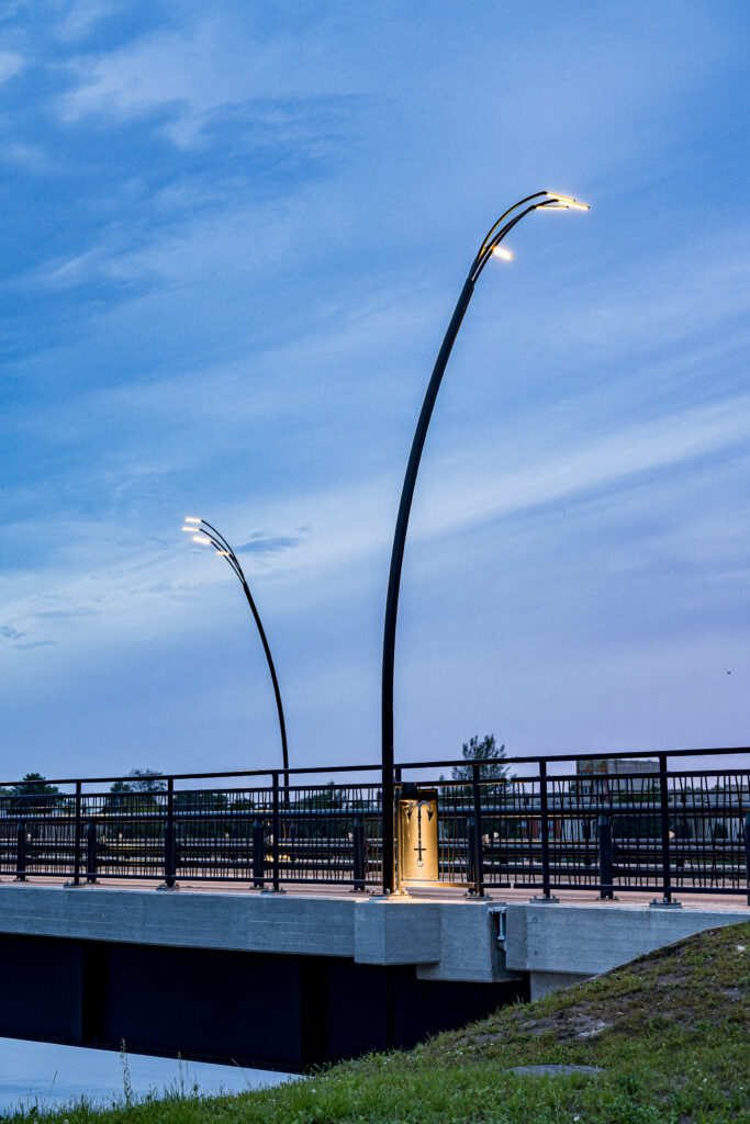 Two Reed luminaires lit at dusk over the bridge, their curved arms outlined against a deepening blue sky.