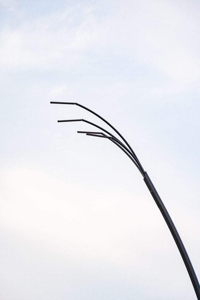 Close detail of a Reed luminaire's branching arms and light heads against a daytime sky.