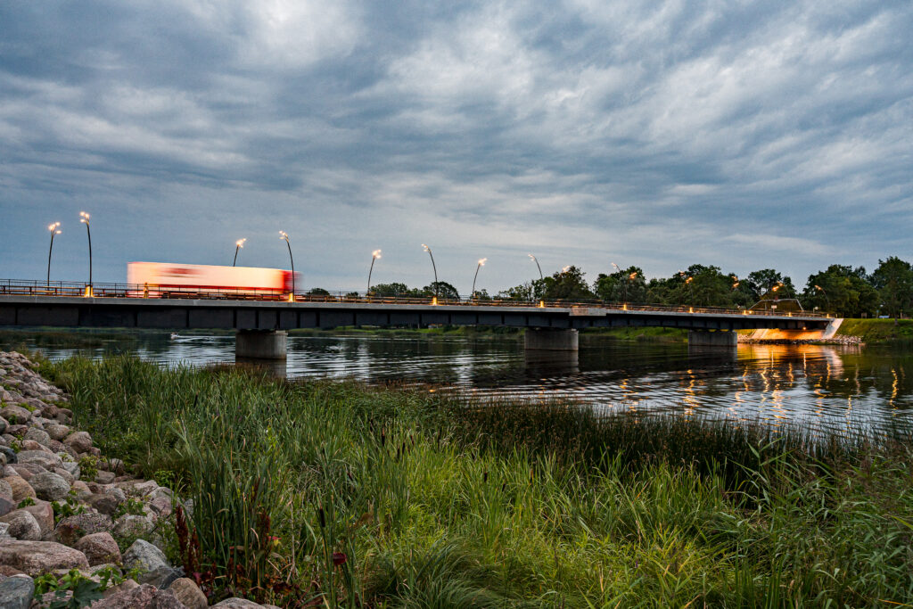 Dramatic evening sky over the Salacgriva bridge, Reed lights glowing as a lorry's headlights streak past.